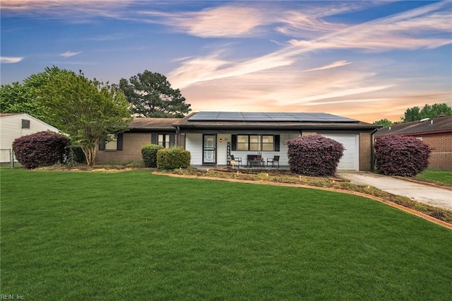 ranch-style home with a lawn, a garage, a porch, and solar panels