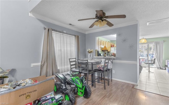 dining space with ceiling fan, light hardwood / wood-style flooring, ornamental molding, and a textured ceiling