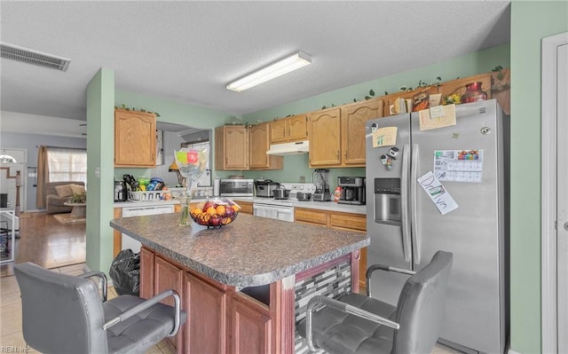 kitchen featuring a textured ceiling, a center island, stainless steel refrigerator with ice dispenser, electric range, and a breakfast bar