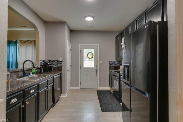 kitchen with tasteful backsplash, dark stone counters, sink, black appliances, and light hardwood / wood-style floors