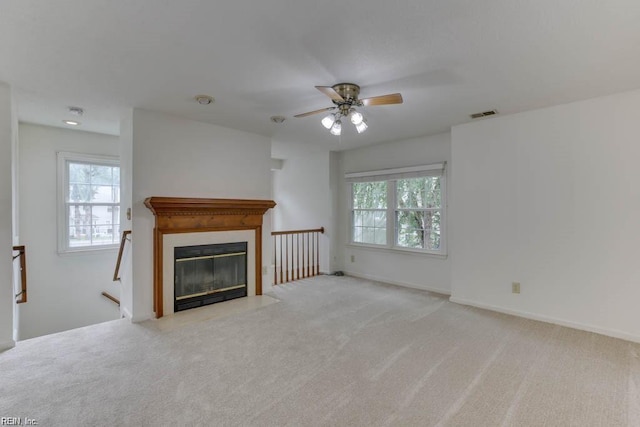 unfurnished living room with light colored carpet, a wealth of natural light, and ceiling fan