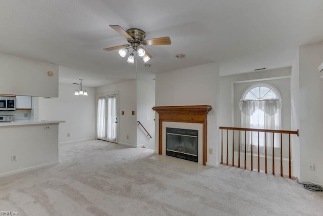 unfurnished living room with ceiling fan with notable chandelier, light colored carpet, and a wealth of natural light