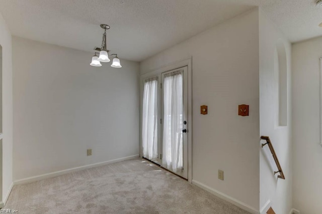 carpeted spare room featuring a textured ceiling and an inviting chandelier