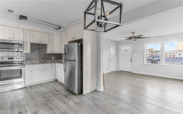 kitchen with ceiling fan with notable chandelier, hanging light fixtures, sink, appliances with stainless steel finishes, and white cabinetry