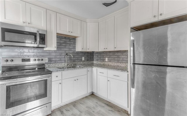 kitchen with appliances with stainless steel finishes, backsplash, light stone counters, sink, and white cabinets