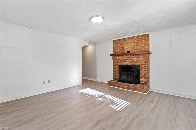 unfurnished living room with light wood-type flooring, crown molding, and a brick fireplace