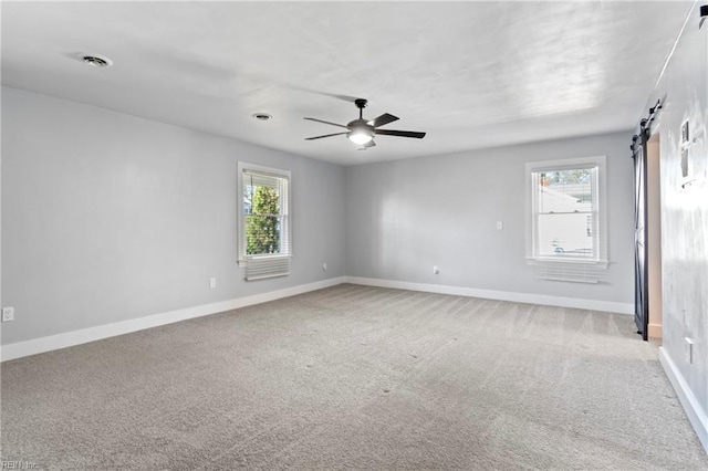 unfurnished room with a barn door, a wealth of natural light, ceiling fan, and light carpet