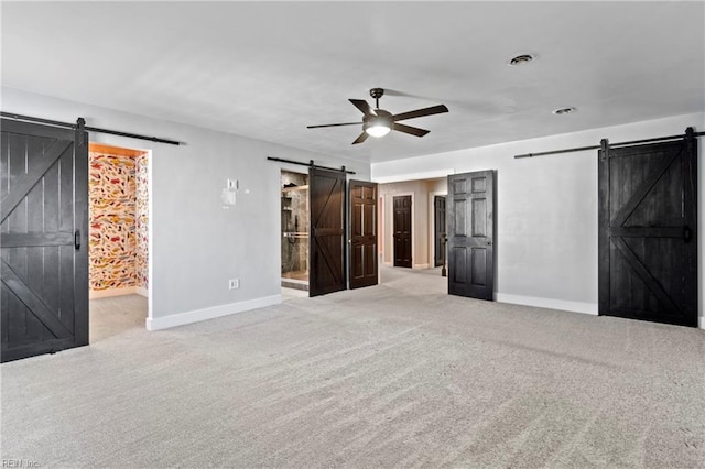 unfurnished bedroom featuring a barn door, ceiling fan, ensuite bath, and light carpet