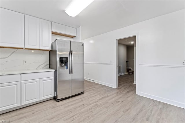 kitchen with white cabinetry, light stone counters, light hardwood / wood-style flooring, stainless steel fridge, and decorative backsplash