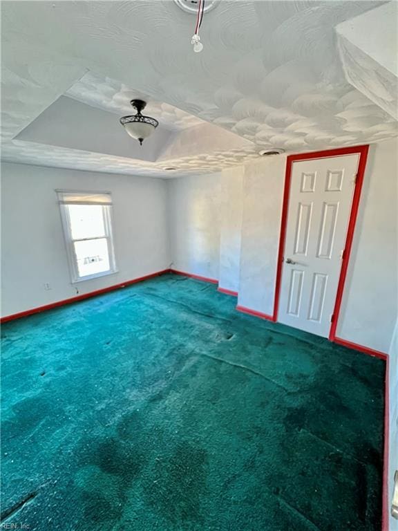 empty room with a raised ceiling and carpet flooring