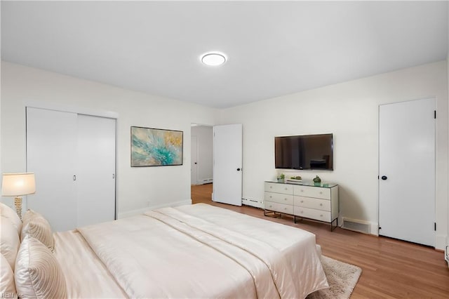 bedroom with light hardwood / wood-style floors, baseboard heating, and a closet