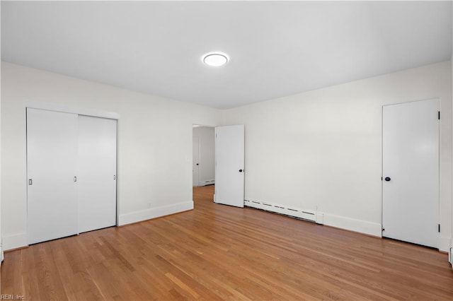 unfurnished bedroom with a closet, light hardwood / wood-style flooring, and a baseboard heating unit