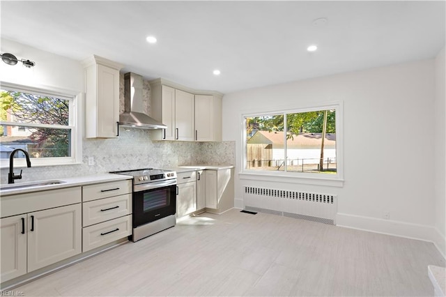 kitchen featuring stainless steel electric range oven, radiator heating unit, sink, wall chimney range hood, and white cabinets