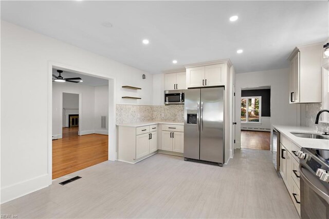 kitchen with appliances with stainless steel finishes, backsplash, sink, light hardwood / wood-style flooring, and white cabinetry