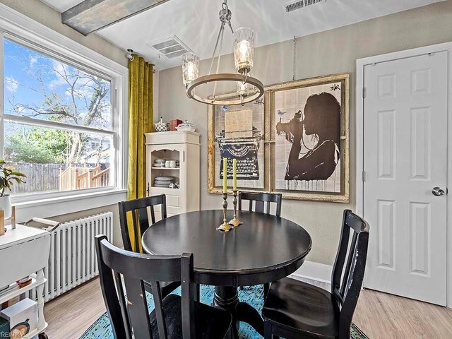 dining space featuring radiator, light wood-type flooring, and a notable chandelier