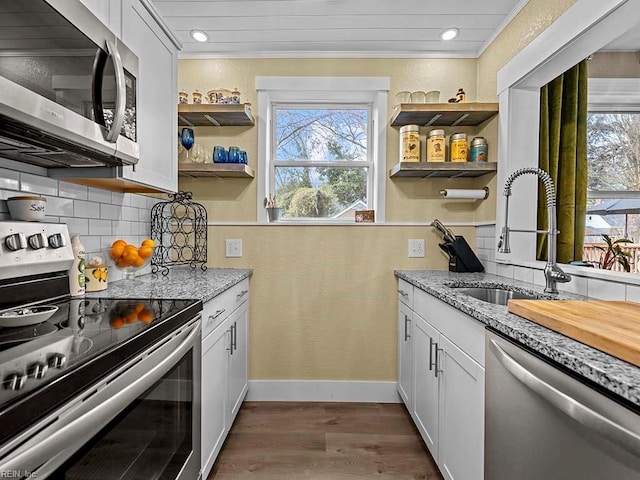 kitchen with light stone counters, stainless steel appliances, dark wood-type flooring, sink, and white cabinets