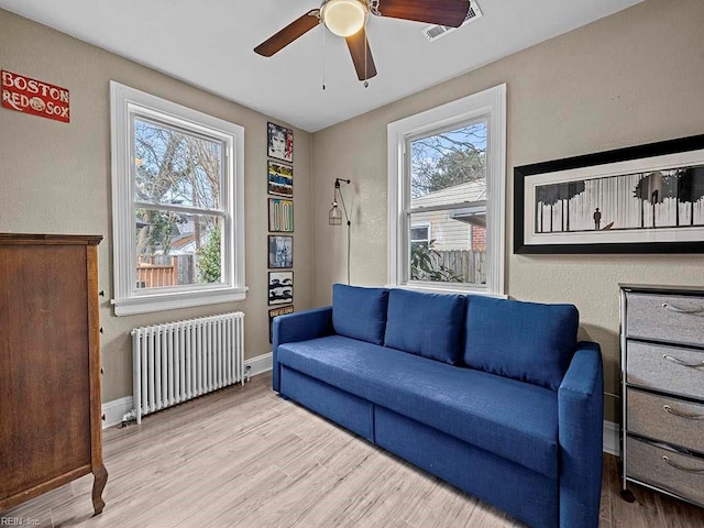 living room featuring a wealth of natural light, light hardwood / wood-style floors, radiator, and ceiling fan