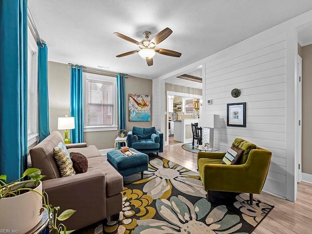 living room featuring light hardwood / wood-style flooring, ceiling fan, and wood walls