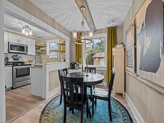 dining area with a chandelier, beam ceiling, and light hardwood / wood-style floors