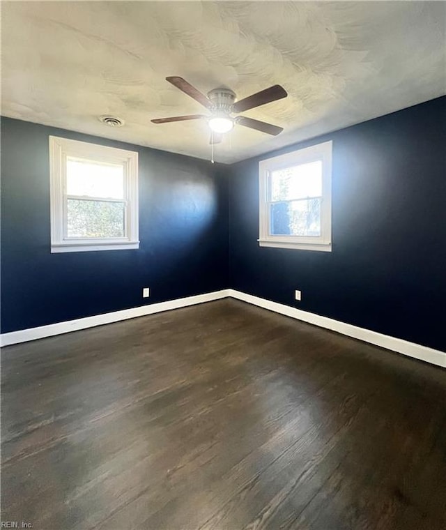 empty room featuring plenty of natural light, ceiling fan, and dark hardwood / wood-style flooring