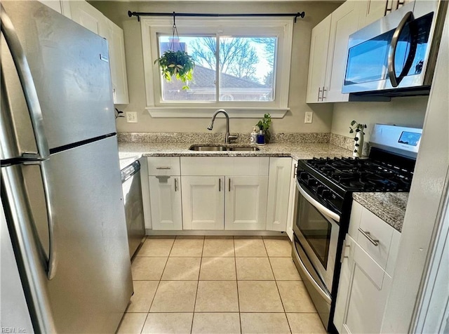 kitchen with light stone countertops, appliances with stainless steel finishes, sink, light tile patterned floors, and white cabinets