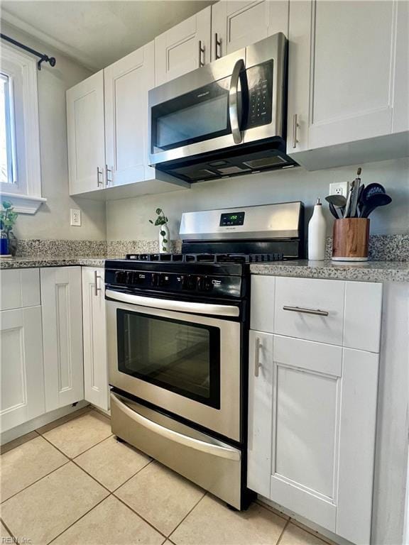 kitchen featuring appliances with stainless steel finishes, light stone counters, white cabinetry, and light tile patterned flooring