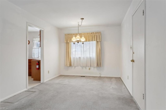 spare room featuring a chandelier and light colored carpet