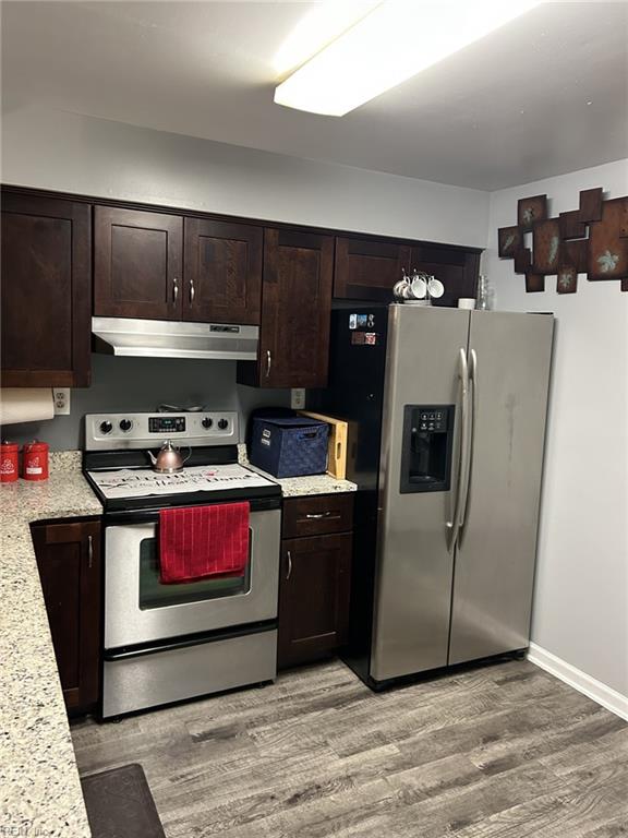 kitchen with dark brown cabinets, light hardwood / wood-style floors, light stone countertops, and stainless steel appliances