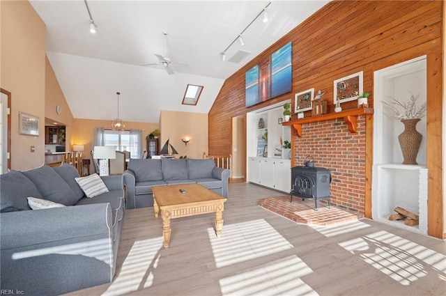 living room featuring a wood stove, wooden walls, high vaulted ceiling, and ceiling fan