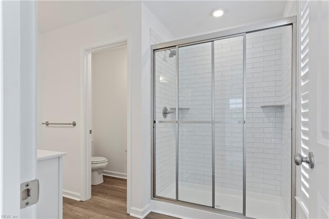 bathroom with wood-type flooring, toilet, and a shower with shower door