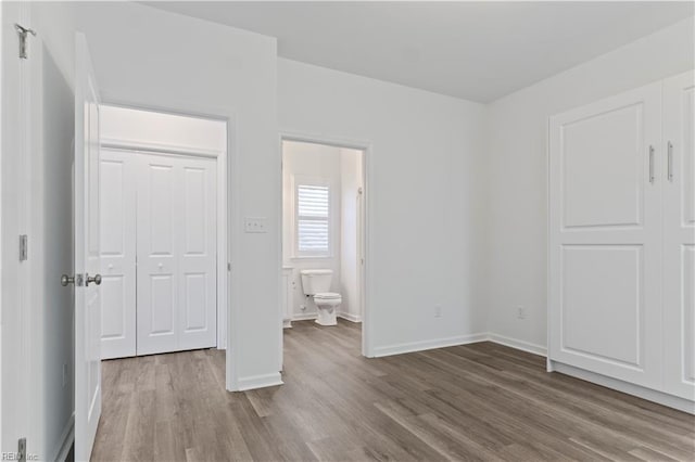 unfurnished bedroom featuring connected bathroom, hardwood / wood-style flooring, and a closet