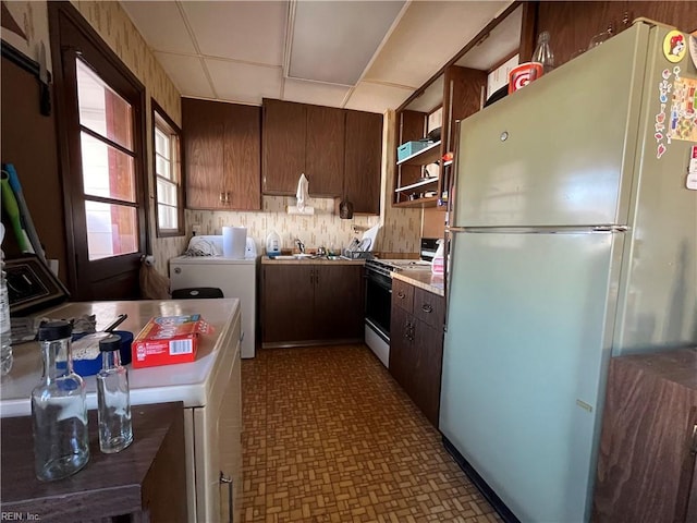 kitchen with dark brown cabinetry, sink, white appliances, and washer / dryer