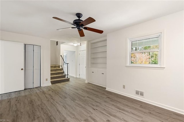 empty room featuring built in shelves, hardwood / wood-style flooring, and ceiling fan