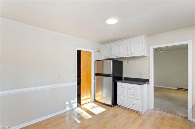 kitchen with white cabinets, light hardwood / wood-style flooring, stainless steel refrigerator, and ornamental molding