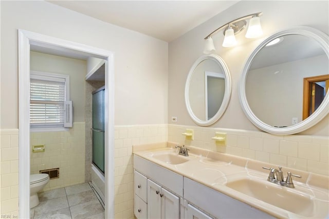 full bathroom with tile patterned flooring, toilet, shower / bath combination with glass door, vanity, and tile walls