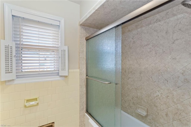 bathroom with shower / bath combination with glass door and tile walls