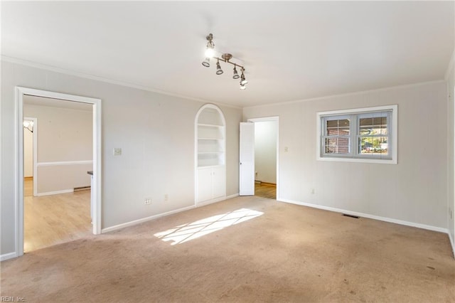 spare room with light colored carpet, ornamental molding, and rail lighting