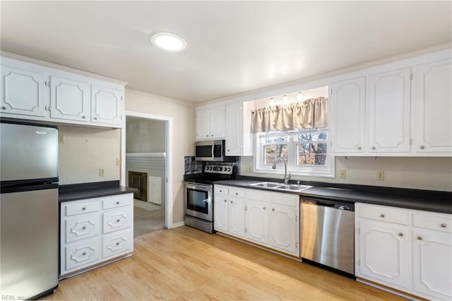 kitchen featuring white cabinetry, sink, stainless steel appliances, light hardwood / wood-style flooring, and backsplash