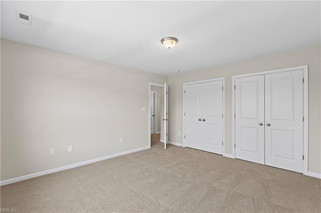 unfurnished bedroom featuring light colored carpet and multiple closets