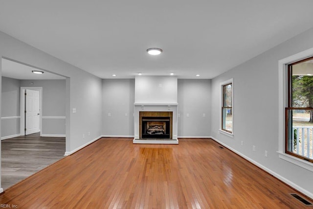 unfurnished living room featuring light wood-type flooring, plenty of natural light, and a tiled fireplace