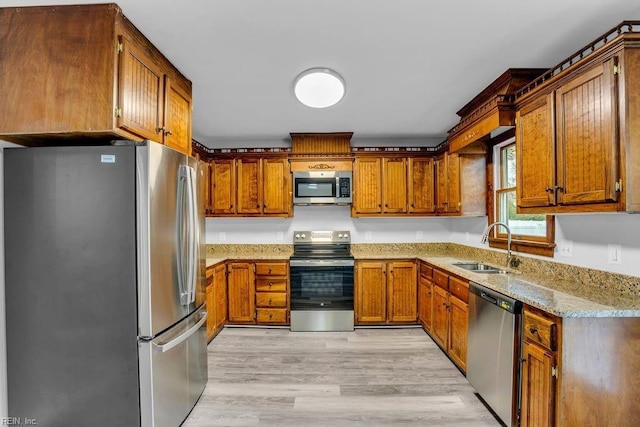 kitchen with light stone countertops, stainless steel appliances, light hardwood / wood-style flooring, and sink