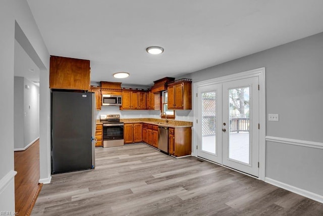 kitchen with appliances with stainless steel finishes, light wood-type flooring, french doors, and sink