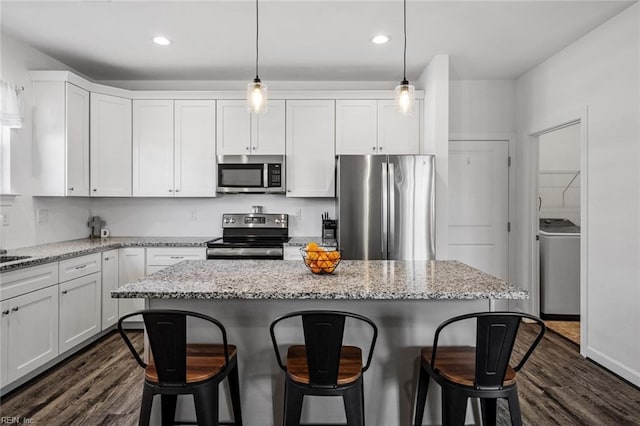 kitchen featuring light stone countertops, appliances with stainless steel finishes, decorative light fixtures, white cabinetry, and washer / clothes dryer