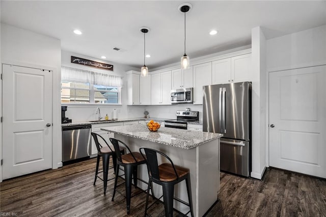 kitchen with a center island, dark wood-type flooring, pendant lighting, white cabinets, and appliances with stainless steel finishes