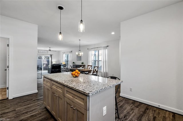 kitchen featuring a center island, a kitchen breakfast bar, light stone counters, decorative light fixtures, and dark hardwood / wood-style flooring