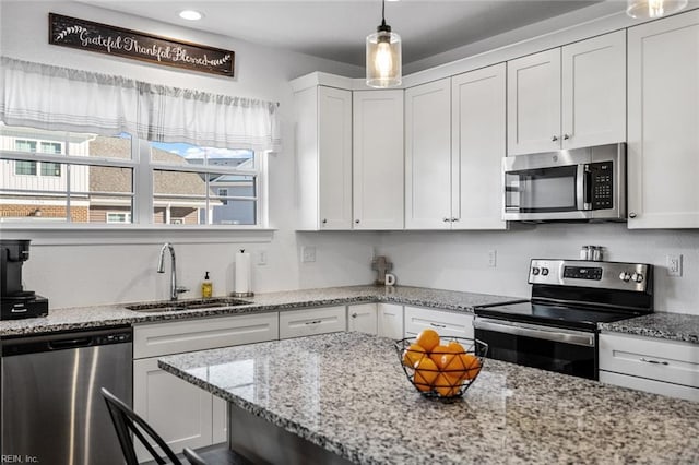 kitchen featuring white cabinetry, sink, hanging light fixtures, light stone counters, and appliances with stainless steel finishes