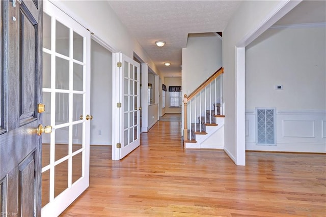 entrance foyer with french doors, a textured ceiling, and light wood-type flooring