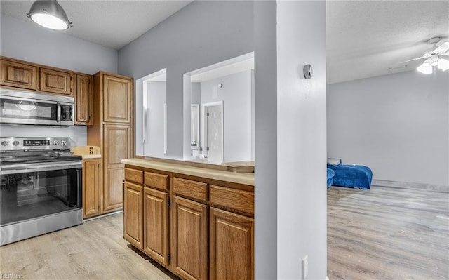 kitchen featuring a textured ceiling, ceiling fan, stainless steel appliances, and light hardwood / wood-style flooring