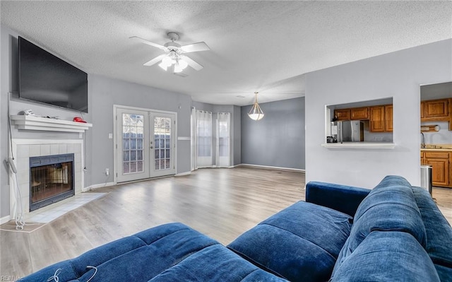 living room featuring french doors, light wood-type flooring, a textured ceiling, ceiling fan, and a fireplace