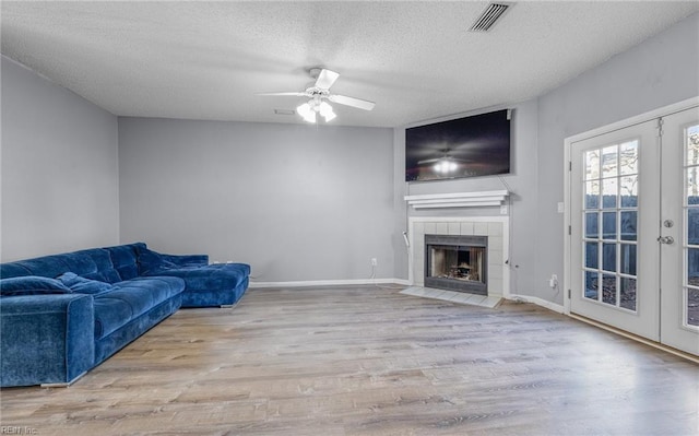 living room with a tile fireplace, french doors, ceiling fan, a textured ceiling, and light hardwood / wood-style floors